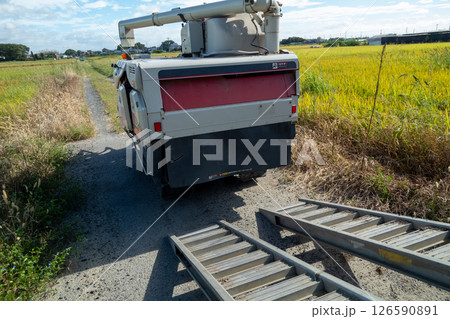 トラックからアユミ板を掛けてコンバインを積み降ろしする 126590891
