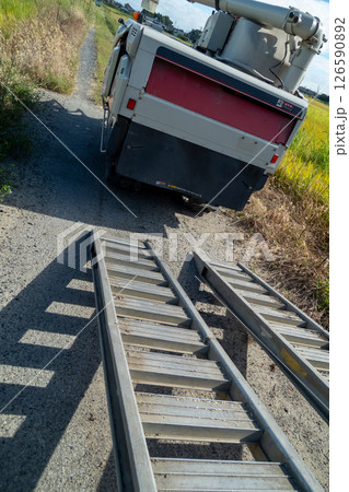 トラックからアユミ板を掛けてコンバインを積み降ろしする 126590892