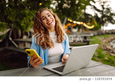 Cute woman in glasses with laptop and smartphone working outdoors. Technology, freelancing. Cute woman in glasses with laptop and smartphone working outdoors. Technology, freelancing. 126593854