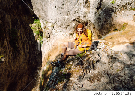 Smiling female traveler with yellow backpack enjoys waterfall near a mountain river. Nature concept. Smiling female traveler with yellow backpack enjoys waterfall near a mountain river. Nature concept. 126594135