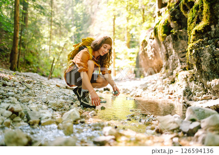 Woman traveler collects water from a stream, climbs up the mountains along a forest hiking trail. 126594136
