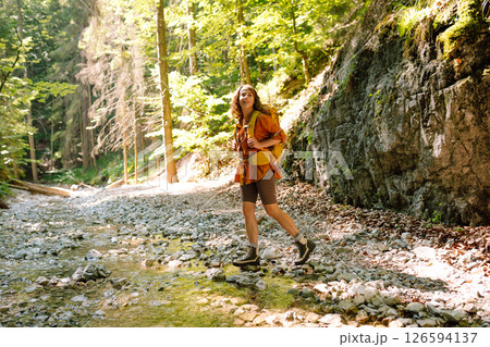Woman traveler collects water from a stream, climbs up the mountains along a forest hiking trail. 126594137