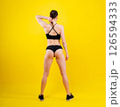 Fit sportswoman in leggings and sports bra looking away and while standing on yellow red 126594333