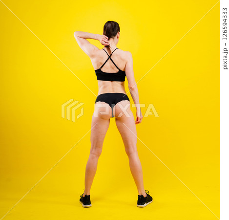 Fit sportswoman in leggings and sports bra looking away and while standing on yellow red Fit sportswoman in leggings and sports bra looking away and while standing on yellow red 126594333