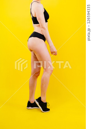Fit sportswoman in leggings and sports bra looking away and while standing on yellow red Fit sportswoman in leggings and sports bra looking away and while standing on yellow red 126594335