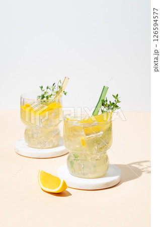 Two glasses of fresh drink lemonade with lemon, thyme and ice on a light background with shadows. Two glasses of fresh drink lemonade with lemon, thyme and ice on a light background with shadows. 126594577
