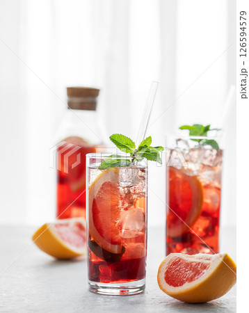 Two glasses of cocktail with grapefruit, mint and ice on a table against a window with natural light Two glasses of cocktail with grapefruit, mint and ice on a table against a window with natural light 126594579