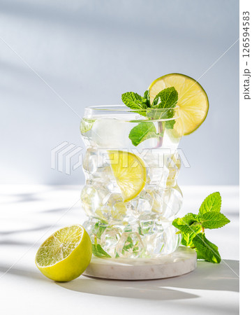 Mojito cocktail in a glass with lime, mint and ice on a white blue background with shadows. Mojito cocktail in a glass with lime, mint and ice on a white blue background with shadows. 126594583