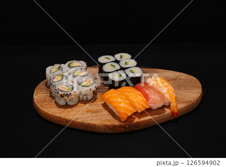 Creative minimalist display of assorted sushi rolls on a wooden platter against a dark backdrop, emphasizing vibrant colors and exquisite Japanese culinary art with a modern aesthetic. 126594902