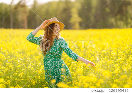 Beautiful woman in bright dress and elegant hat walks and has fun in rapeseed field. Nature, rest. 126595453