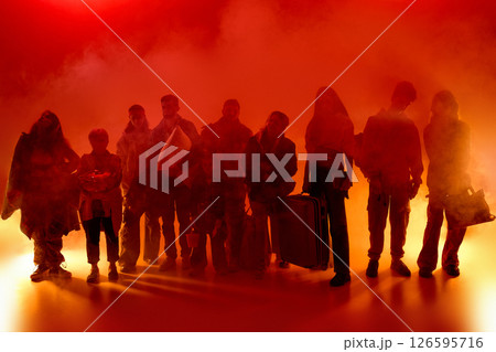 Group of people stands in thick fog with bright red neon glow, holding bags and pillows, staring ahead. Forced movement 126595716