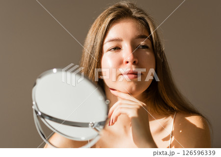 Cute woman with rashes on her face looks into small mirror. Natural skin without filter. Cosmetology Cute woman with rashes on her face looks into small mirror. Natural skin without filter. Cosmetology 126596339