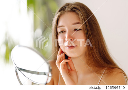 A beautiful woman looking in mirror, examines acne, pigmentation. Cosmetic care. Allergic reaction. 126596340
