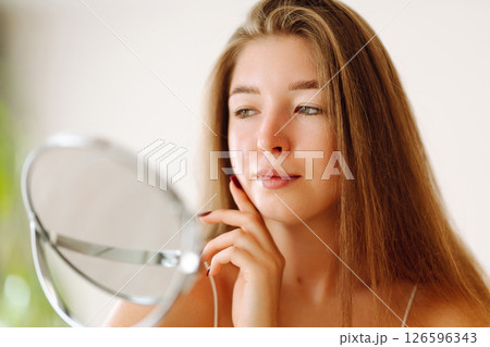 A beautiful woman looking in mirror, examines acne, pigmentation. Cosmetic care. Allergic reaction. 126596343