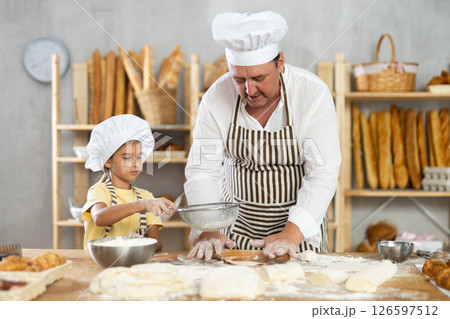 Bakers dad teaches daughter niece to work with dough, using rolling pin Bakers dad teaches daughter niece to work with dough, using rolling pin 126597512