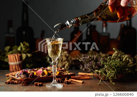 Yellow herbal liquor or mixture is poured from a vintage bottle into a glass. Yellow herbal liquor or mixture is poured from a vintage bottle into a glass. 126600840
