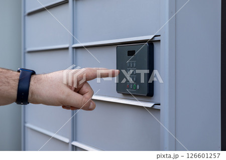 Customer hand touching digital keypad for code entry on automated parcel locker providing secure package delivery access 126601257