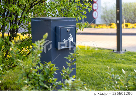 Dark grey public pet waste bin with person and dog icon provides designated disposal point in outdoor urban environment promoting cleanliness and hygiene standards Dark grey public pet waste bin with person and dog icon provides designated disposal point in outdoor urban environment promoting cleanliness and hygiene standards 126601290