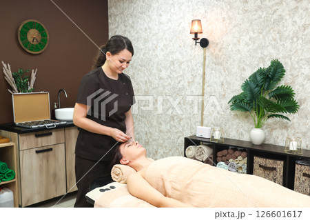 A female massage therapist gently begins a forehead massage on a lying client of the salon 126601617