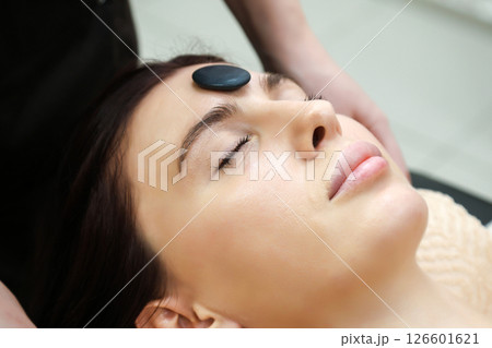 Black round basalt stone for massage lies on woman's forehead 126601621