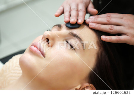 Black round basalt stone for massage lies on woman's forehead Black round basalt stone for massage lies on woman's forehead 126601622