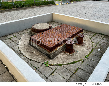 Rusty weathered urban manhole covers and smaller access caps set in concrete and paving provide essential entry points for maintenance of underground utility infrastructure systems 126602202