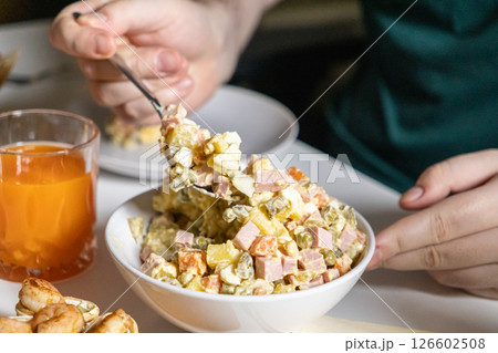 person scooping Olivier salad from a bowl, creamy texture with diced ham, potatoes, carrots, pickles, and mayonnaise dressing 126602508