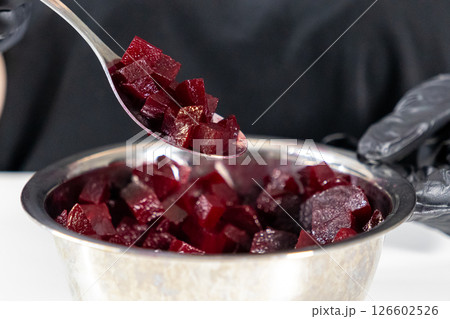 freshly chopped beetroot in a spoon over a metal bowl, preparing ingredients for homemade vinaigrette or other salads, chef wearing black gloves 126602526