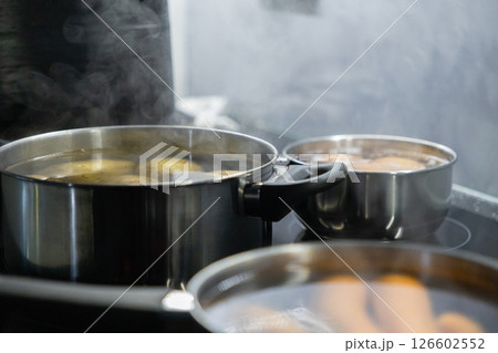 three pots with boiling potatoes, eggs, and carrots on a stovetop, steam rising as ingredients cook for a homemade meal preparation three pots with boiling potatoes, eggs, and carrots on a stovetop, steam rising as ingredients cook for a homemade meal preparation 126602552