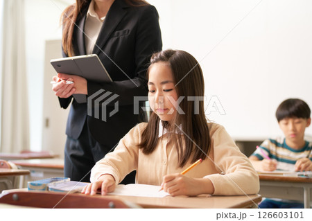 勉強している小学生と見守る先生 勉強している小学生と見守る先生 126603101