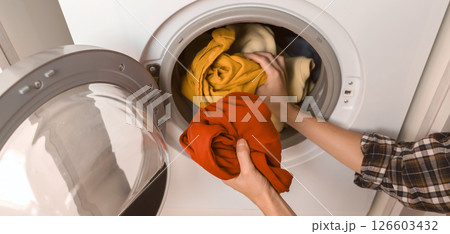 Woman puts bright clothes into a washing machine. 126603432