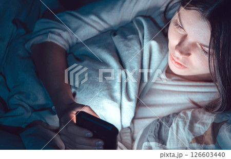 Young girl in a bed with a phone at night. 126603440