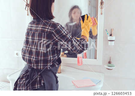 Young woman is washing mirror in the bathrom. Young woman is washing mirror in the bathrom. 126603453