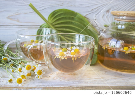 Herbal medicinal tea with chamomile flowers in a glass teapot, a bouquet of fresh flowers, on a wooden light background. Herbal medicinal tea with chamomile flowers in a glass teapot, a bouquet of fresh flowers, on a wooden light background. 126603646