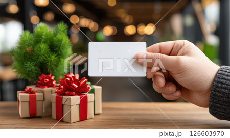 Hand holding blank card with Christmas gifts and festive bokeh background 126603970