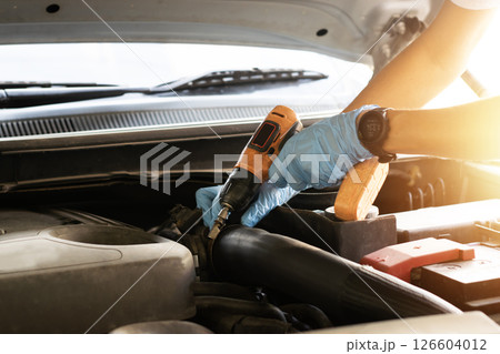 The mechanic is fixing the engine, using an electric screwdriver to tighten the screws. 126604012
