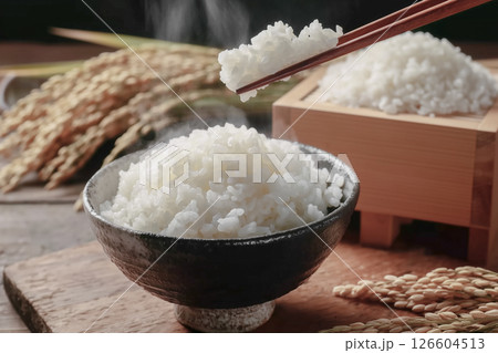 ご飯茶碗に盛られた湯気の立ち上る白米を箸で持ち上げる。背景は稲穂。日本の和食イメージ 126604513