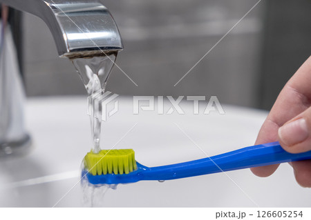 Brushing teeth with running water from a faucet for effective dental hygiene and daily oral care routine Brushing teeth with running water from a faucet for effective dental hygiene and daily oral care routine 126605254
