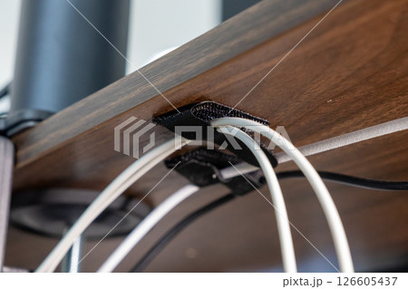 cable management under wooden desk using black velcro straps, showcasing organized wiring setup for efficient workspace arrangement, close-up view cable management under wooden desk using black velcro straps, showcasing organized wiring setup for efficient workspace arrangement, close-up view 126605437