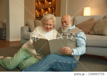 Cheerful loving elderly married couple watching album with memory photo 126605759