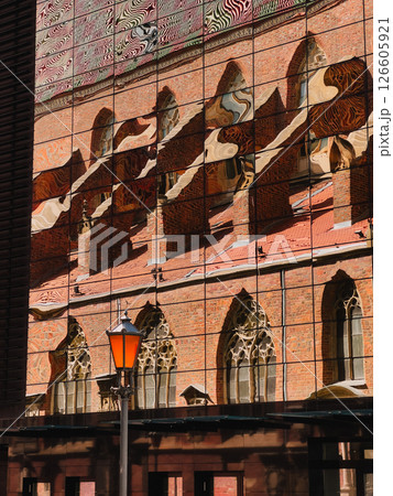 Distorted reflection of old red brick church with arched windows and tiled roof on modern glass building facade with orange street lamp in foreground. Warped mirror, red cathedral, orange streetlight Distorted reflection of old red brick church with arched windows and tiled roof on modern glass building facade with orange street lamp in foreground. Warped mirror, red cathedral, orange streetlight 126605921