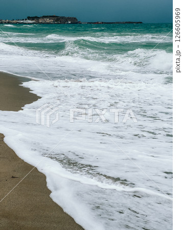 Powerful white foamy waves breaking against sandy shoreline during stormy weather, revealing intense coastal seascape with dramatic cloudy sky and turbulent ocean dynamics. White foamy sea, cloudy day Powerful white foamy waves breaking against sandy shoreline during stormy weather, revealing intense coastal seascape with dramatic cloudy sky and turbulent ocean dynamics. White foamy sea, cloudy day 126605969