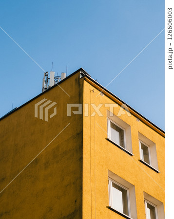 Low angle view capturing a vibrant yellow building corner adorned with antennas on the rooftop, set against a clear blue sky, enhancing telecommunication services in the urban landscape. yellow, blue Low angle view capturing a vibrant yellow building corner adorned with antennas on the rooftop, set against a clear blue sky, enhancing telecommunication services in the urban landscape. yellow, blue 126606003