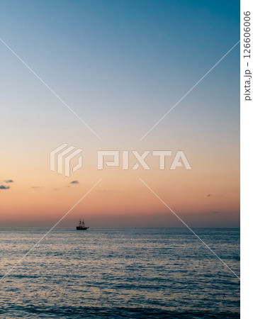 Wooden galleon sailing across tranquil ocean waters, golden sunset casting warm orange and pink light, evoking maritime history and serene nautical atmosphere. Galleon sails away on calm sea, sun sets 126606006