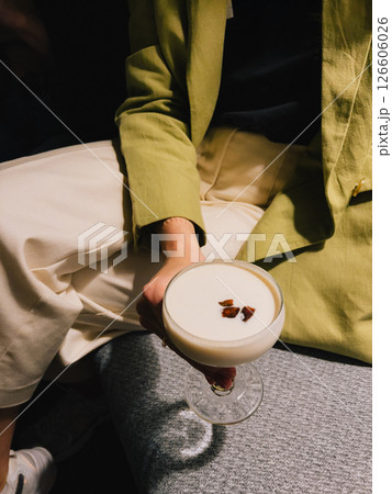 POV shot: woman in green jacket sitting comfortably on sofa, holding cocktail glass filled with creamy alcoholic beverage, beautifully garnished with chocolate, enjoying relaxed evening 126606026
