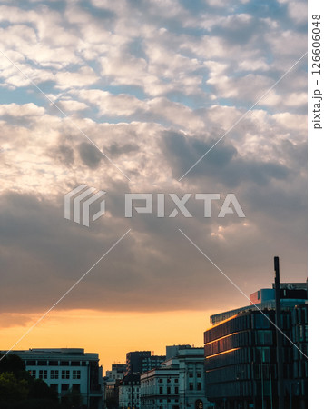 Skyline reflecting orange sunset light under cloudy sky with modern and historical buildings at golden hour in city. Cityscape glows with warm sunset, blending contemporary and historic architecture 126606048