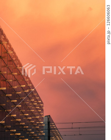 Glass facade of contemporary building reflecting warm orange hues of sunset sky, creating striking and vibrant architectural scene in urban cityscape. Glass facade reflecting warm orange sunset hues Glass facade of contemporary building reflecting warm orange hues of sunset sky, creating striking and vibrant architectural scene in urban cityscape. Glass facade reflecting warm orange sunset hues 126606063