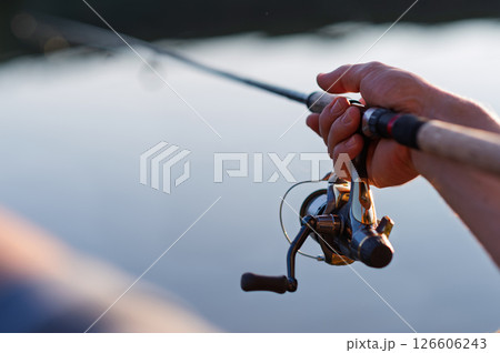 Peaceful evening fishing scene with detailed shots of hands holding rod. 126606243