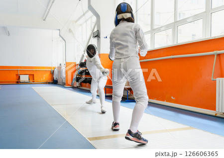 Female fencer lunging toward opponent in bright fencing hall. 126606365