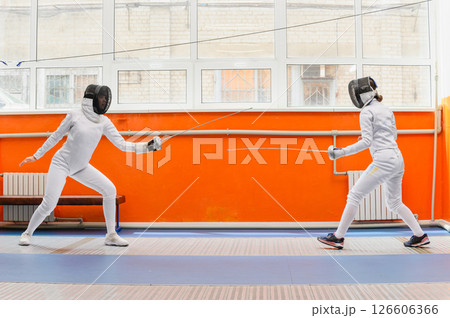 Female fencers preparing to attack in bright fencing hall. Female fencers preparing to attack in bright fencing hall. 126606366